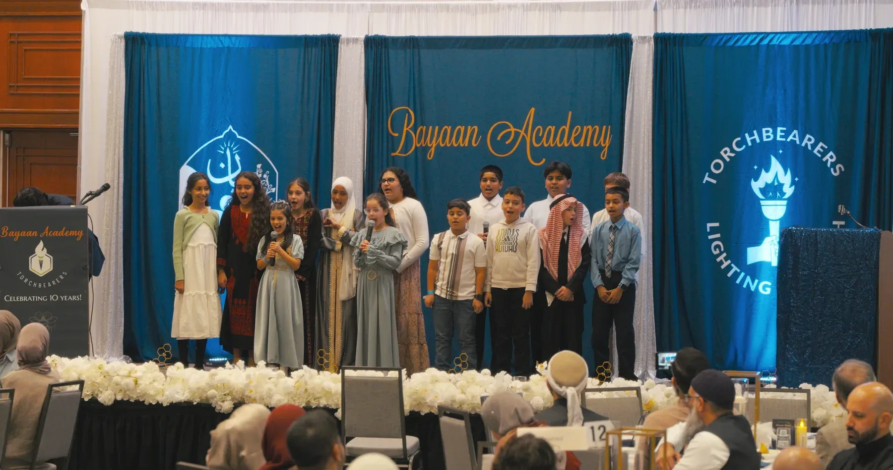 Bayaan Academy students and adults gathered onstage during a fundraising event