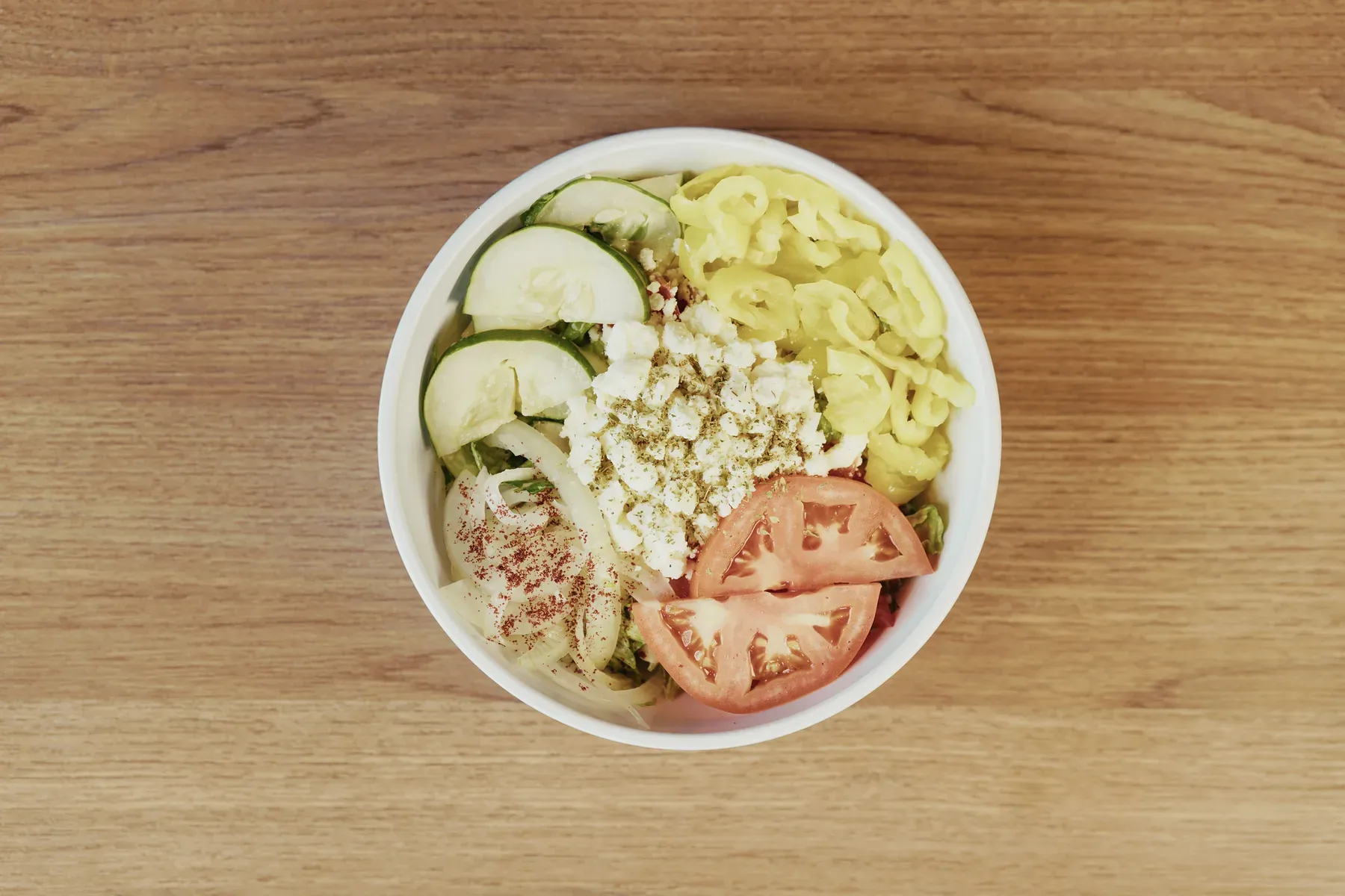 Top-down photograph of a Mediterranean salad with tomatoes, cucumbers, onions, peppers, and cheese