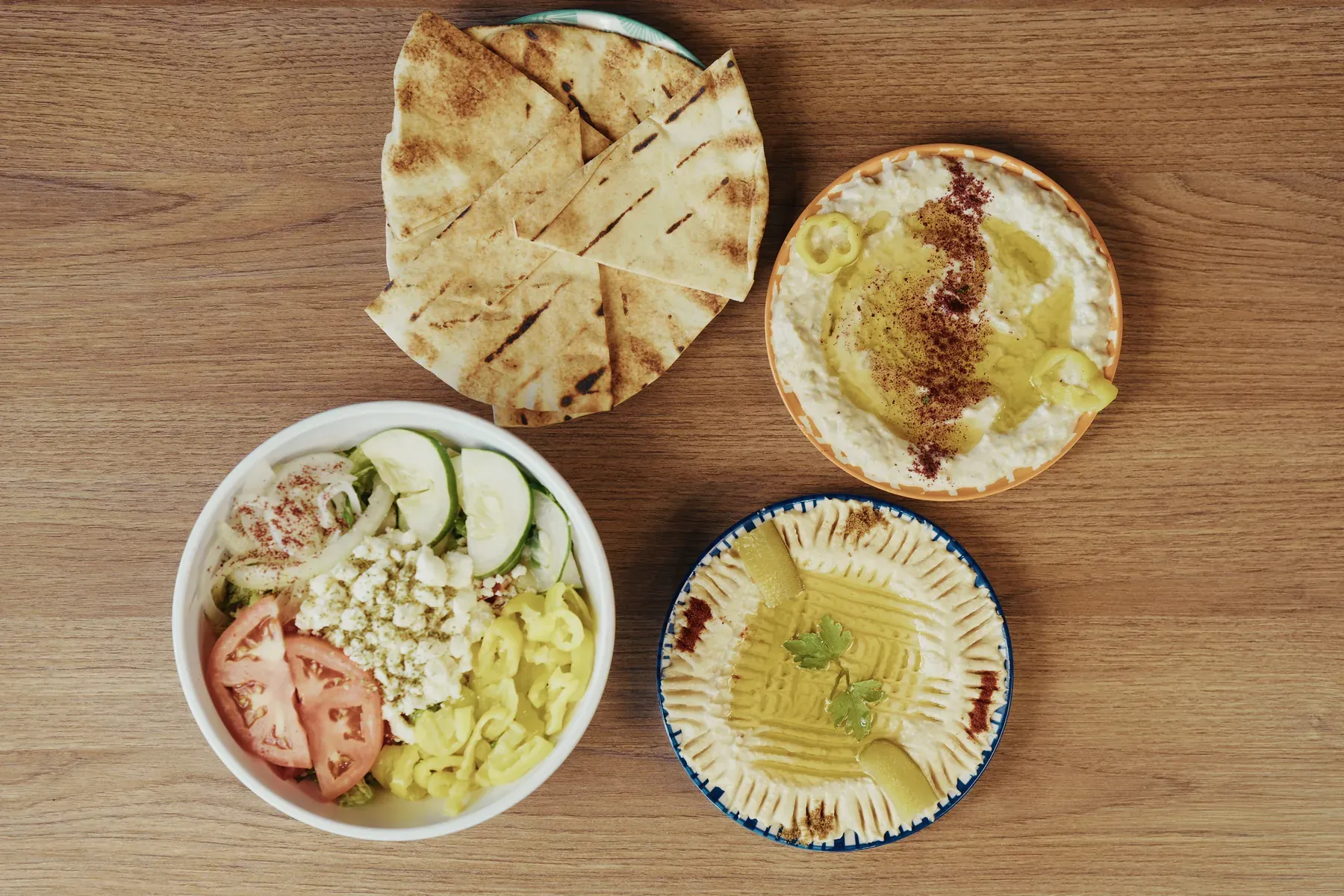 Overhead arrangement of pita bread, hummus, baba ghanoush, and a fresh Mediterranean salad