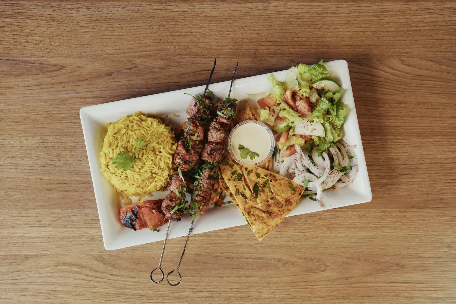 Grilled beef skewers served with rice, salad, seasoned pita bread, and sauce