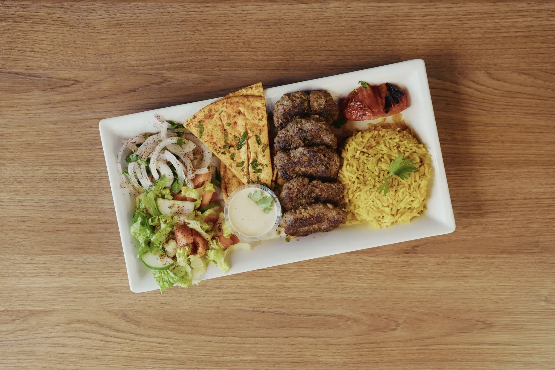 Grilled kafta patties served with rice, salad, seasoned pita bread, tomato, and sauce