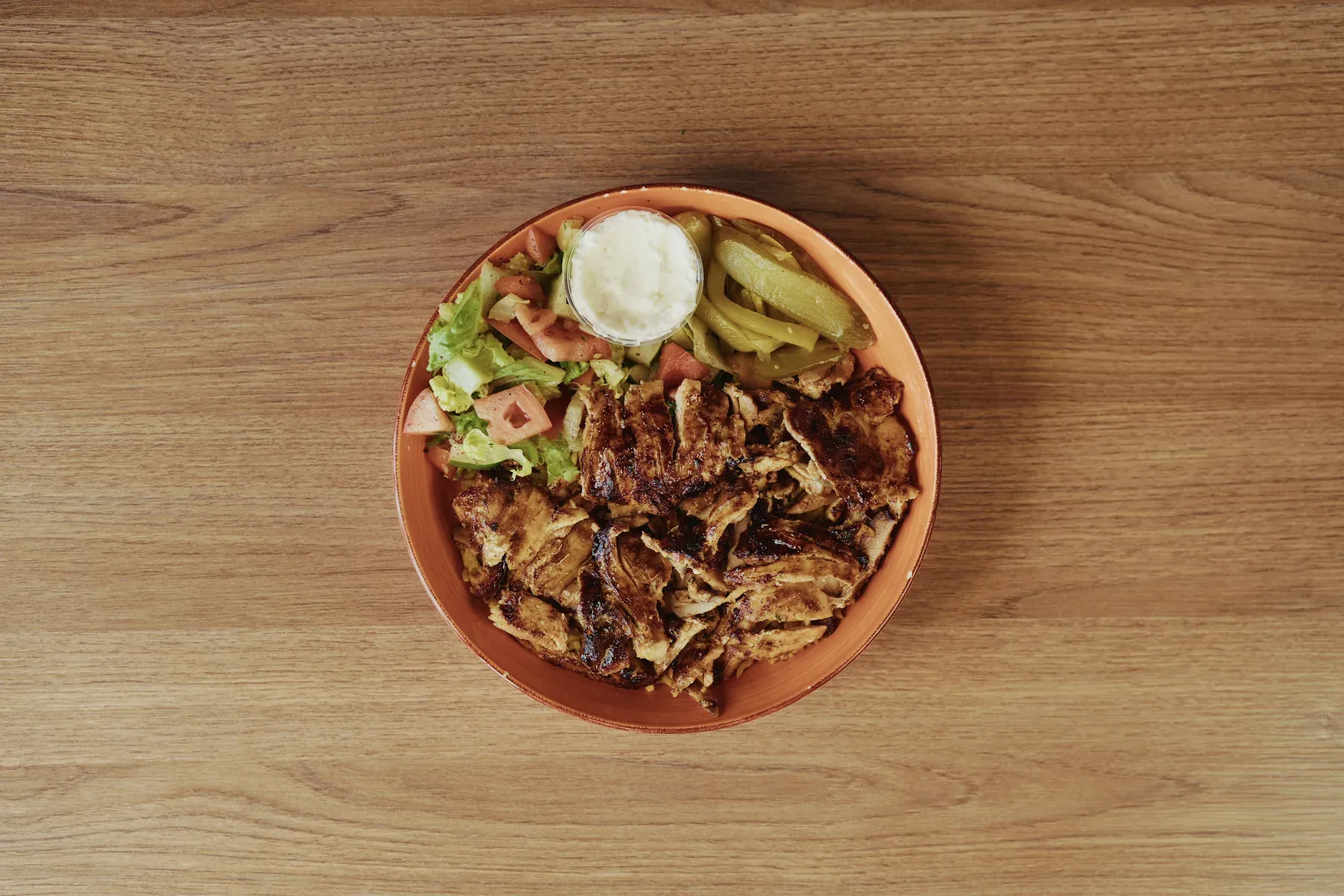 Overhead bowl of grilled chicken with salad, pickled vegetables, and garlic sauce