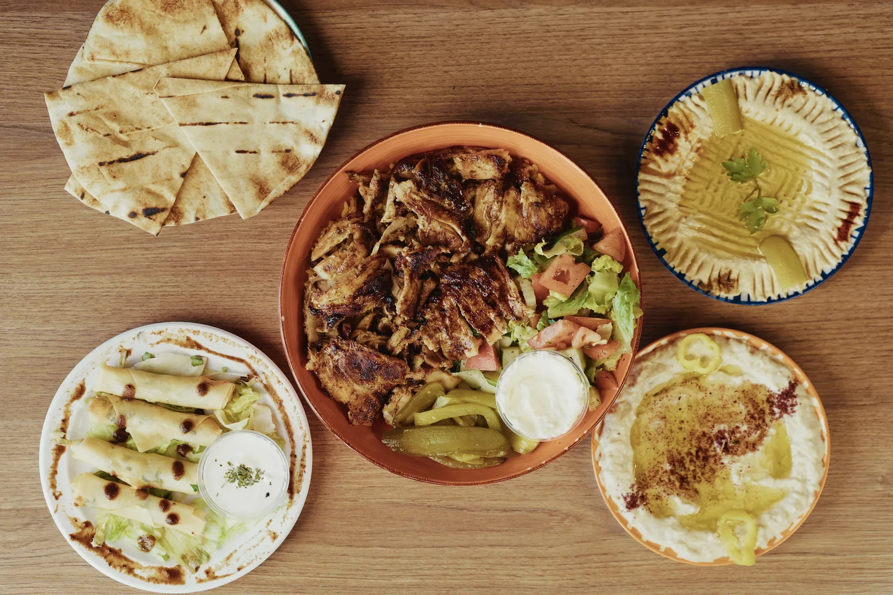 Overhead spread of grilled chicken, hummus, baba ghanoush, pita bread, and cheese rolls at Al Forno Lebanese Grill