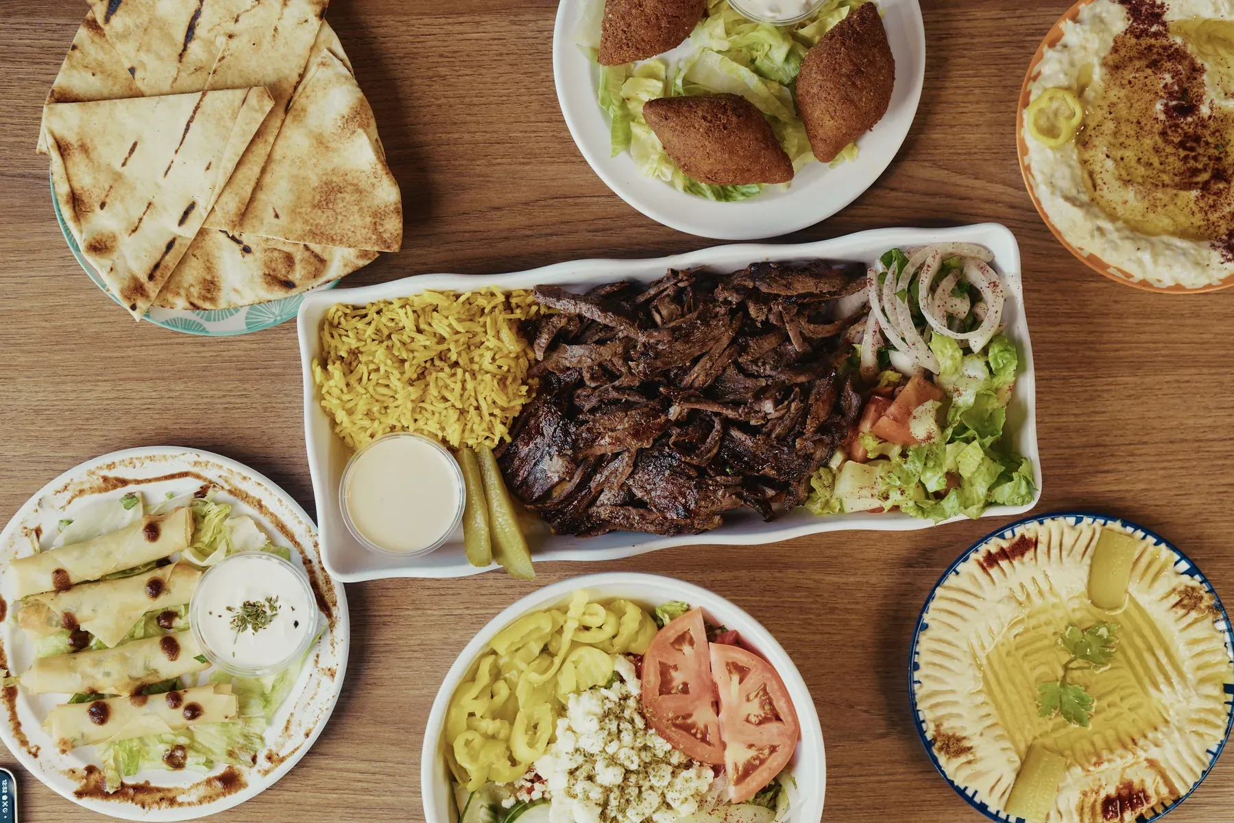 Beef shawarma platter surrounded by hummus, baba ghanoush, kibbeh, salad, cheese rolls, and pita bread