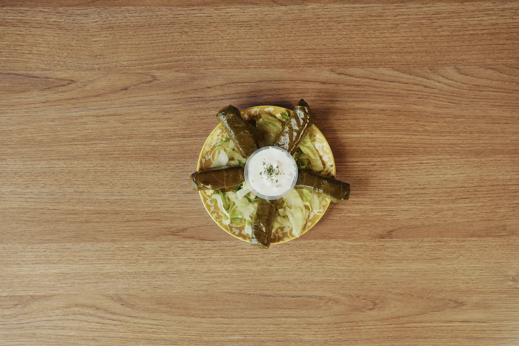 Stuffed grape leaves arranged around a cup of yogurt sauce