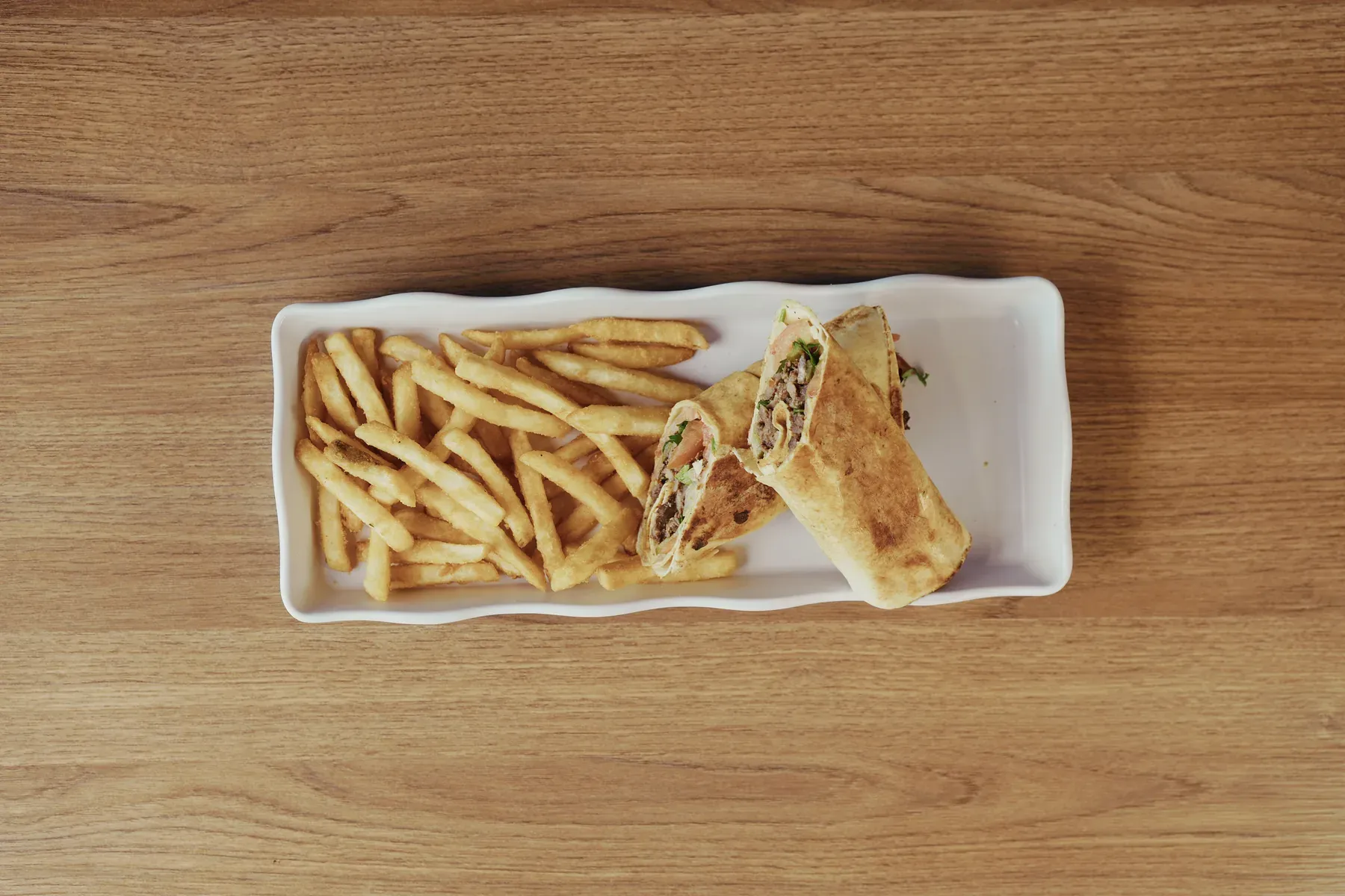 Grilled wrap cut open and served with french fries on a rectangular plate