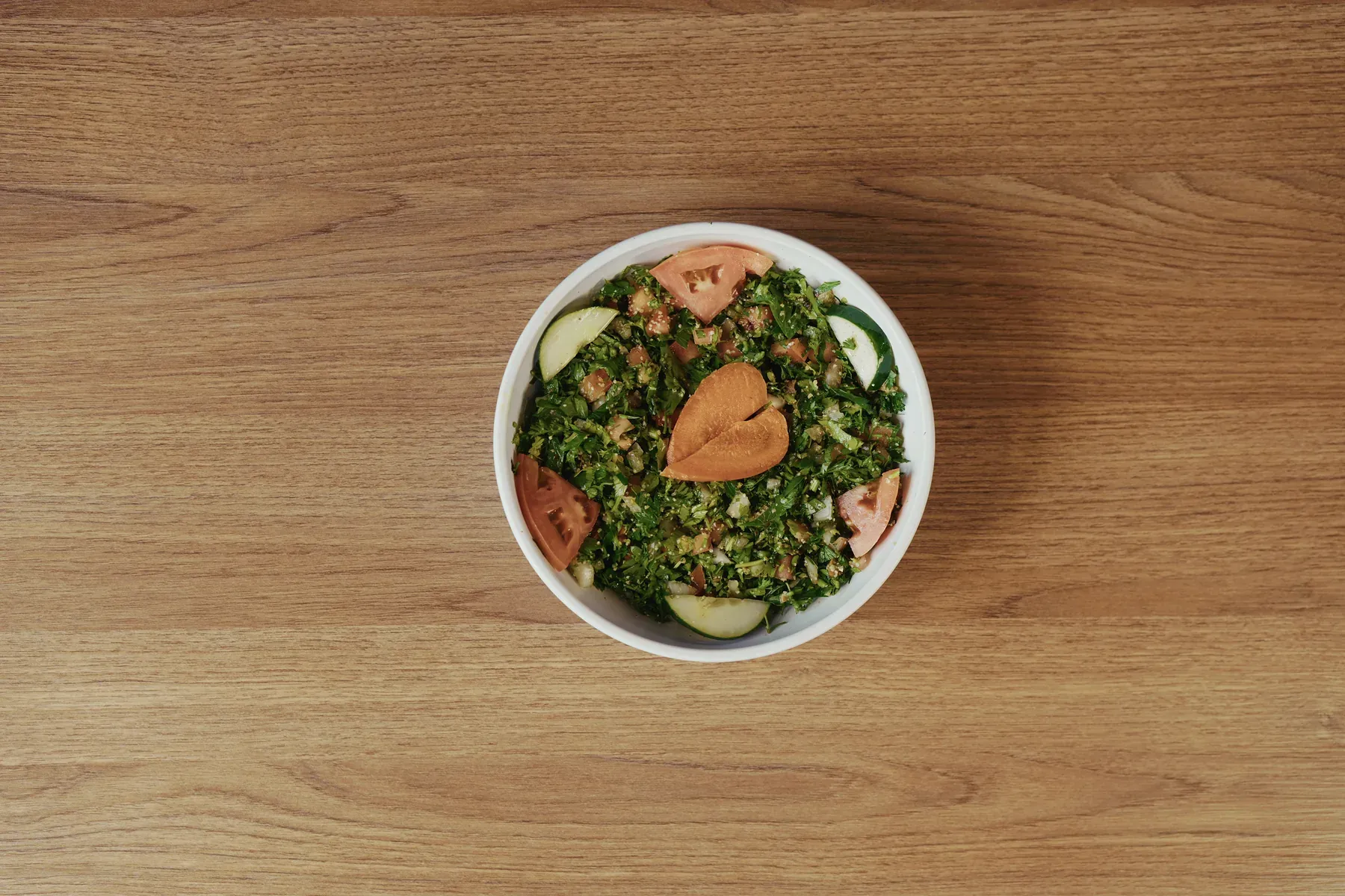 Bowl of tabbouleh garnished with tomato, cucumber, and crisp pita pieces