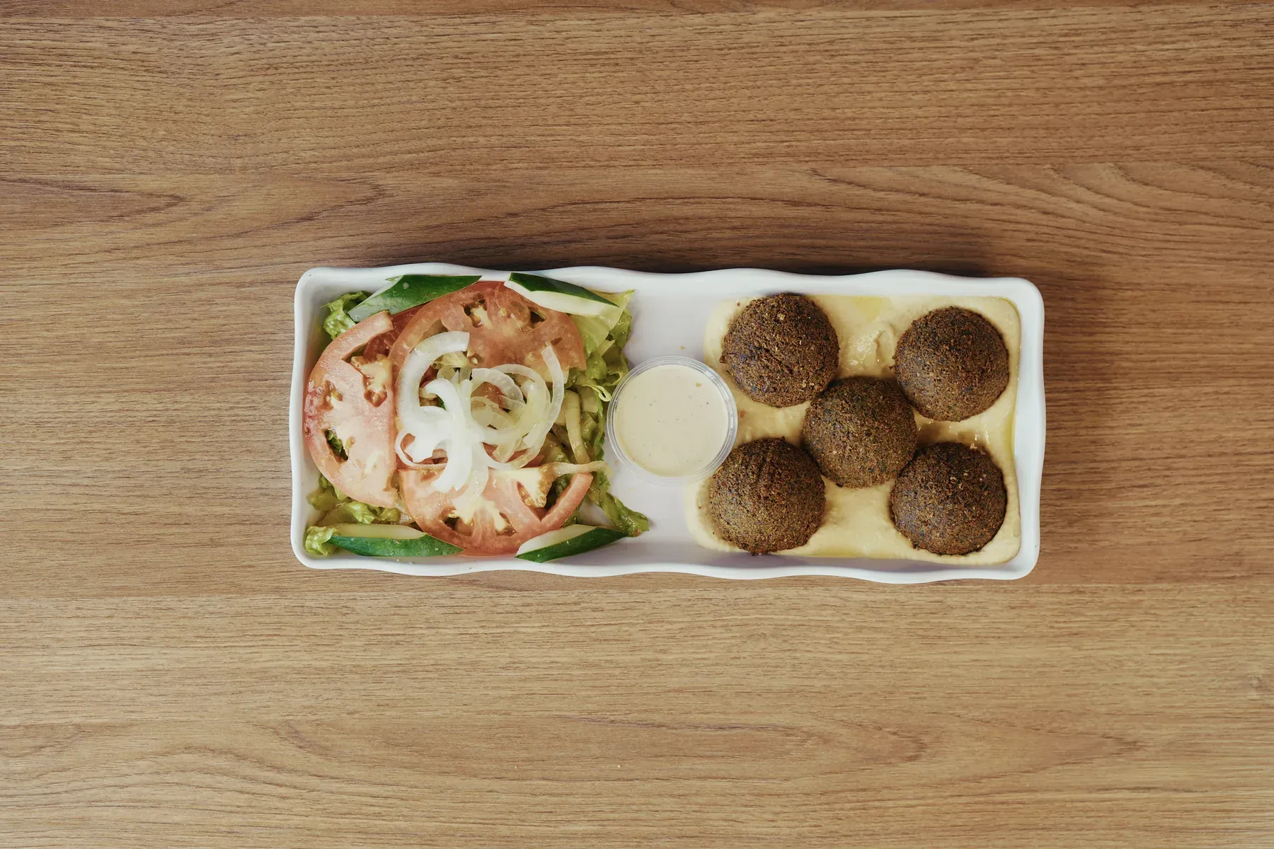 Falafel served over hummus with salad and tahini sauce