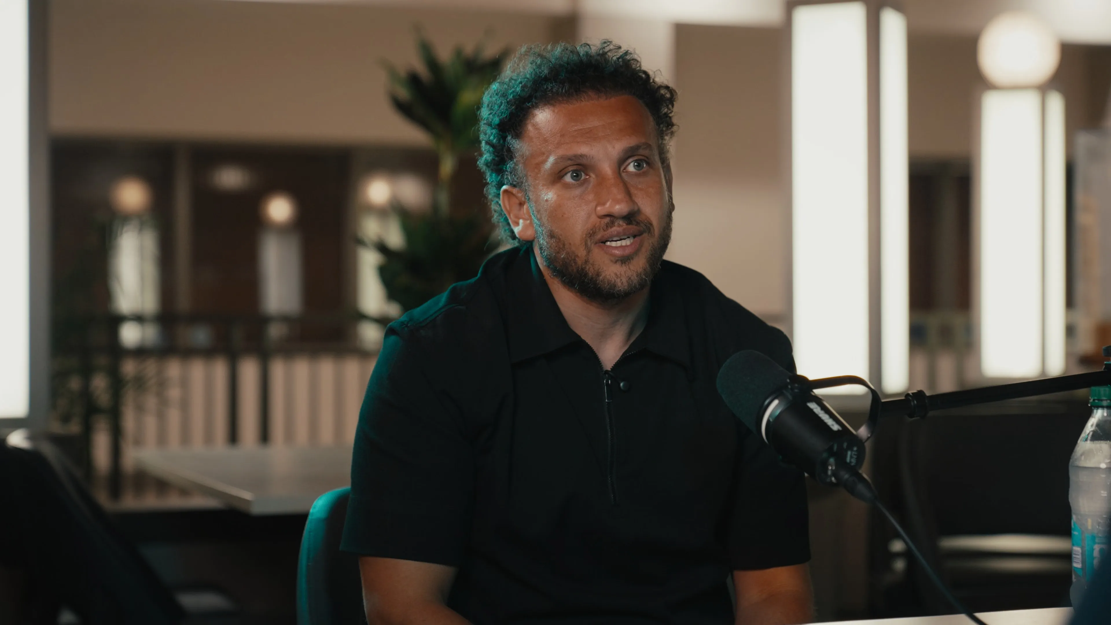Youssef Hussein speaking into a Shure MV7+ microphone with soft facial light and a teal rim light along his hair and shoulder